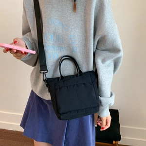 Detail of a black nylon crossbody bag with adjustable strap worn by a female model
