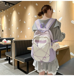 Student backpack in purple and white patchwork with a cute plush pendant on a model