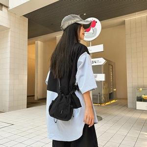 Street style shot of a black nylon drawstring crossbody bucket bag with mesh side pockets