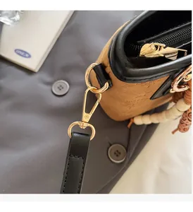 Close-up of golden hardware, suede texture and bead charm on a brown crossbody bag