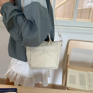 Detail of a cream nylon crossbody bag in a minimalist indoor setting with soft lighting