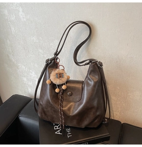 Close-up of dark brown soft leather tote bag with lion plush pendant on a book