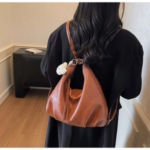 Detail of caramel brown ruched leather shoulder bag with a cute white teddy bear charm