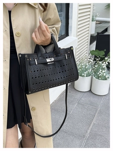 Detailed close-up of black perforated leather handbag with silver metallic turn-lock closure