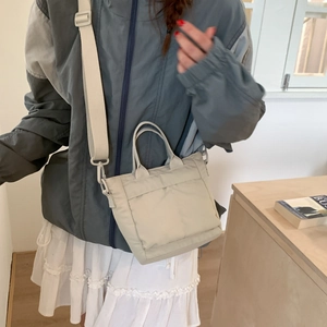Detail of a beige nylon crossbody bag with adjustable strap and multiple utility pockets