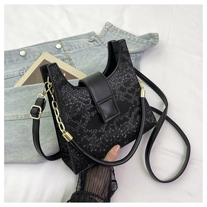 Detail of black snakeskin embossed handbag with gold chain strap and square buckle