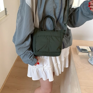 Detail view of the dark green quilted nylon crossbody bag shown in a cozy indoor setting