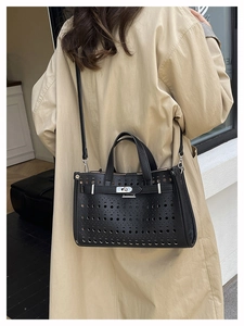 Close-up of black perforated leather tote with metal turn-lock and adjustable straps
