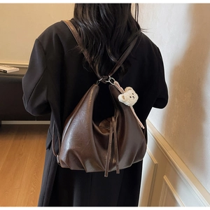 Detail of dark brown glossy leather tote bag with a cute white plush bear pendant