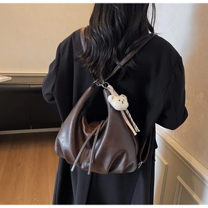 Detail view of the deep brown leather texture and cute white bear charm on the backpack