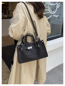 Close-up of black laser-cut hollow pattern and leather strap buckle on a tote bag