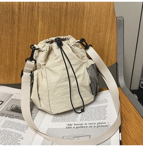 Detail shot of a beige nylon bucket bag with drawstring and side mesh pocket