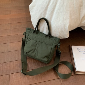 Close-up of army green nylon tote bag with wide strap on a white bed in home setting