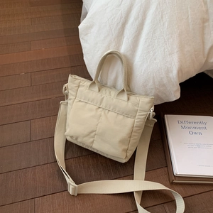 Close-up of cream-colored nylon tote bag with adjustable strap on a wood floor