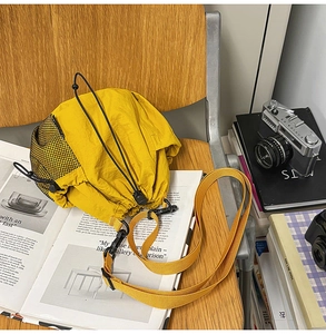 Detail of yellow nylon bucket bag with mesh pocket and drawstring on a wooden chair