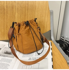 Close-up of tan nylon bucket bag with drawstring closure and mesh side pocket on a magazine