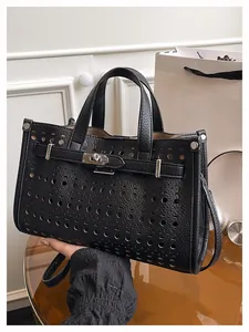 Detail of black lychee grain leather tote featuring circular hollow perforations and lock