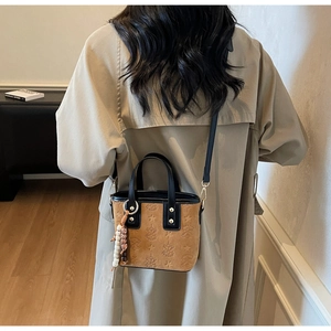 Detail of tan bucket bag with star embossing and ethnic beaded charm on the side