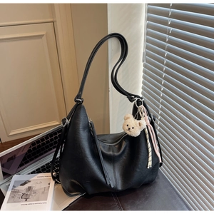 Detail of a black matte leather hobo bag with plush bear charm on a leather seat