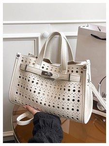 Close-up of white leather tote bag featuring laser-cut circular patterns and silver buckle