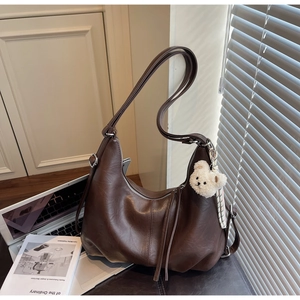 Close-up of hobo bag in brown matte leather with a cute plush bear charm decoration