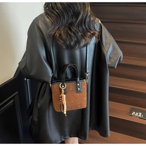 Detail of a brown suede bucket bag with embossed star patterns and beaded tassel charm