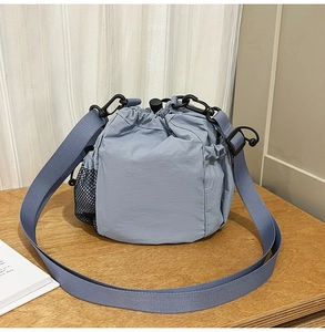 Detail of blue nylon drawstring bucket bag with mesh pocket on light wood surface