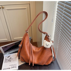 Close-up of hobo bag in orange-brown lychee leather with white bear charm and fringe zipper