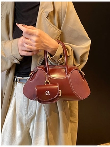 Deep burgundy leather handbag with white stitching and mini charm on trench coat