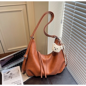 Brown crescent shoulder bag with plush bear charm and sleek leather texture close-up