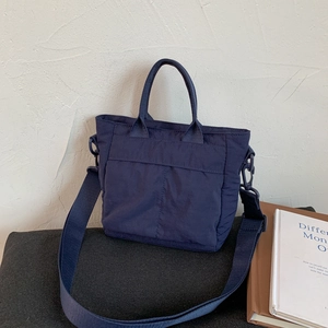Close-up of a navy blue quilted nylon crossbody bag with handles on a minimalist background
