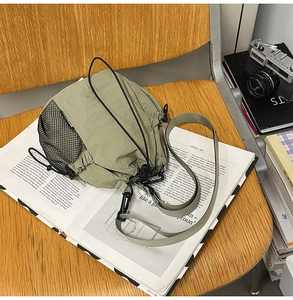 Detail of green nylon drawstring bucket bag with black mesh pocket on wooden chair