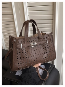 Close-up of laser-cut hollow details on dark brown lychee leather tote with silver buckle