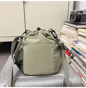 Detail view of light green nylon drawstring bucket bag with black mesh side pocket and strap