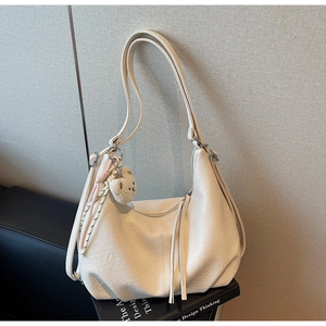 Detail of off-white hobo shoulder bag featuring a cute plush bear charm and tassel zipper