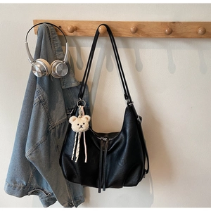Detail of a large black faux leather hobo bag with a white plush bear charm on a wooden rack