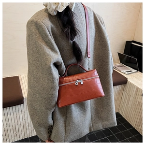 Detail view of reddish-brown crocodile texture leather bag with silver zippers and top handle