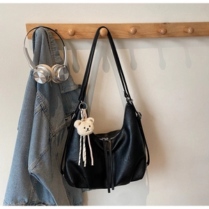 Detail of black faux leather hobo bag hanging on a wooden hook with a cute bear charm