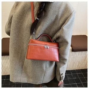 Detail view of terracotta crocodile-embossed handbag featuring dual silver zippers