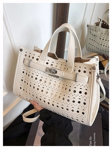 Detail of laser-cut perforated pattern on cream-white structured tote bag with metal buckle