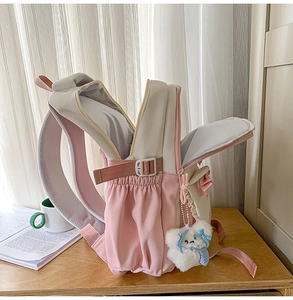 Close-up of pink and beige backpack showing side buckle straps and plush bear charm