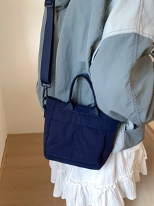Navy blue nylon mini tote bag with adjustable strap worn as crossbody for casual look