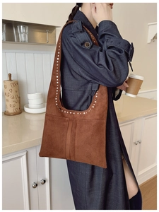 Détail du sac bandoulière en daim marron avec rivets argentés porté par un mannequin