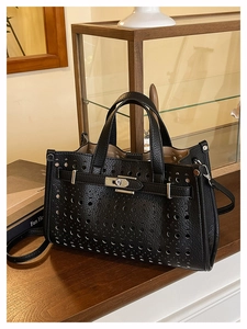 Detail of black hollow-out tote bag featuring lychee pattern and silver turn-lock closure