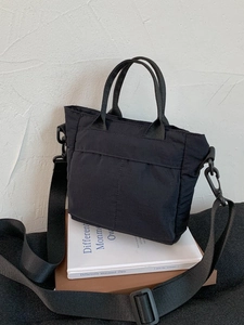 Minimalist black nylon crossbody bag with adjustable wide strap on a book base