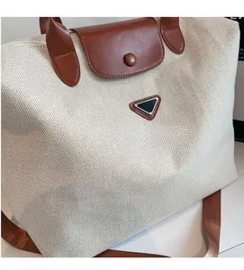 Close-up of canvas tote bag showing brown leather handles and triangle metal logo detail