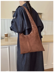 Sac hobo en daim marron avec clous argentés porté par un mannequin en trench denim