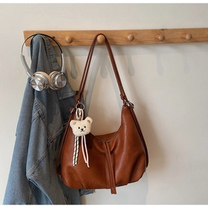 Detailed close-up of brown PU leather tote bag with plush bear charm and ribbon