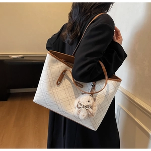 Dettaglio borsa shopper a scacchi bianchi con manici in pelle marrone e ciondolo
