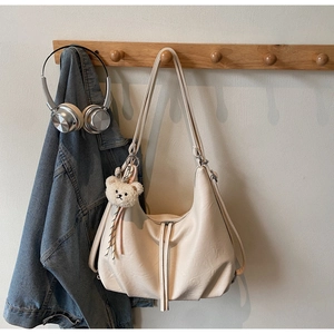 Detail of a creamy white hobo bag with dual zipper straps and a cute plush bear charm